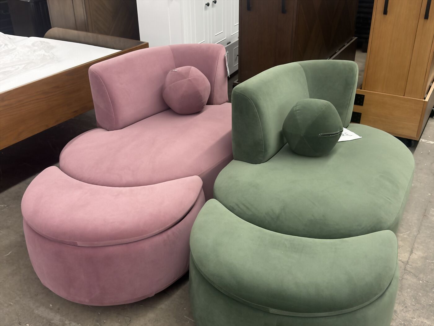 A blush pink swivel chair and an olive green swivel chair with matching ottomans on a warehouse floor.