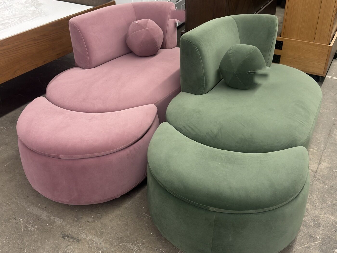 A pink and a sage-green swivel chaise, each with a round bolster cushion.