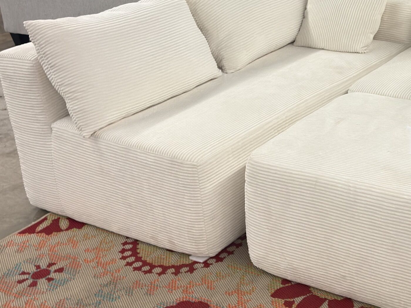 A cream wide-wale corduroy modular sofa with deep back cushions and a matching ottoman.