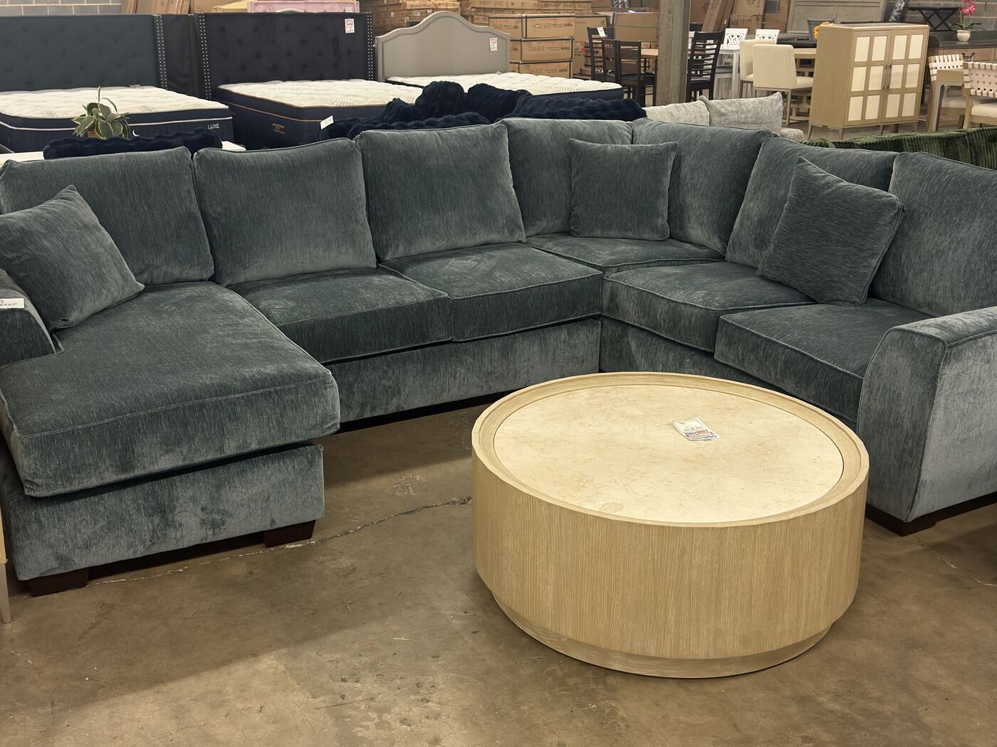 A teal chenille sectional with a deep chaise, beside a round light-oak coffee table.