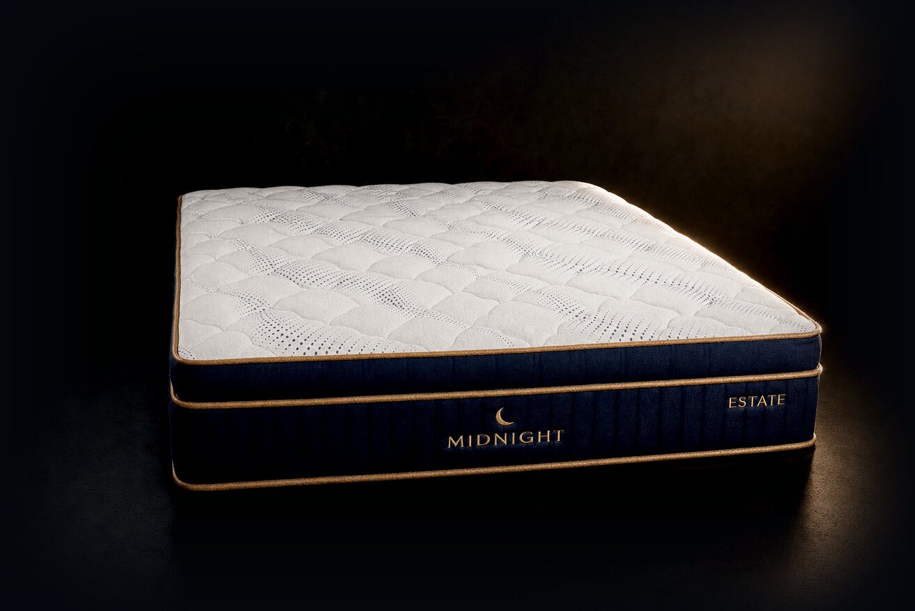 Our house-label mattress in three-quarter view: a white quilted top over a navy border with gold piping.