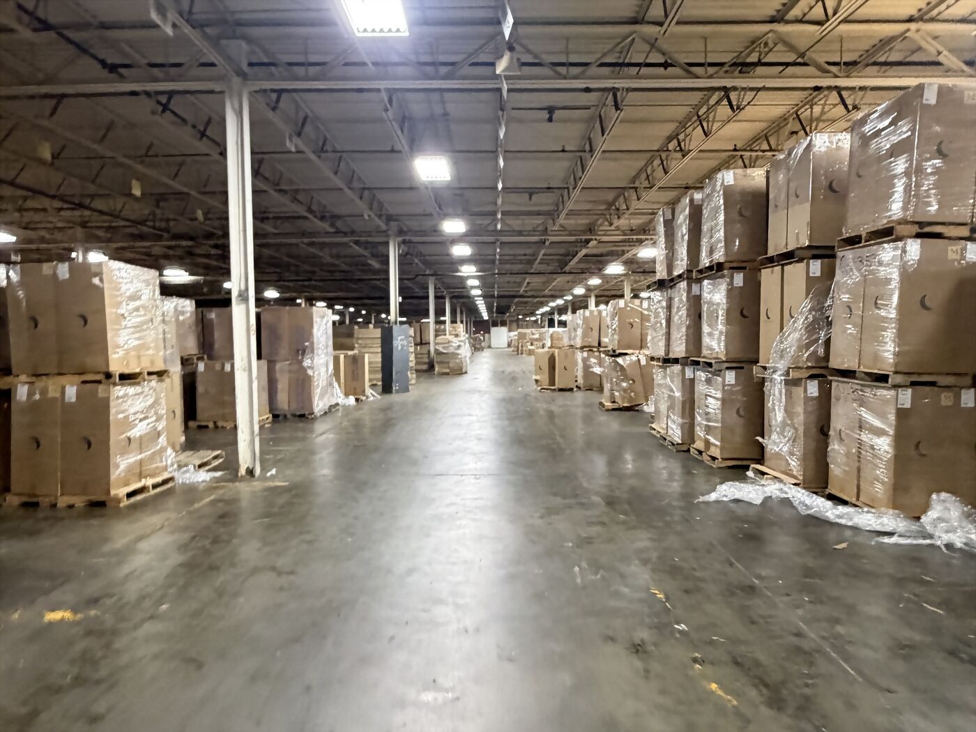 A long warehouse aisle with wrapped and boxed stock stacked on pallets down both sides.