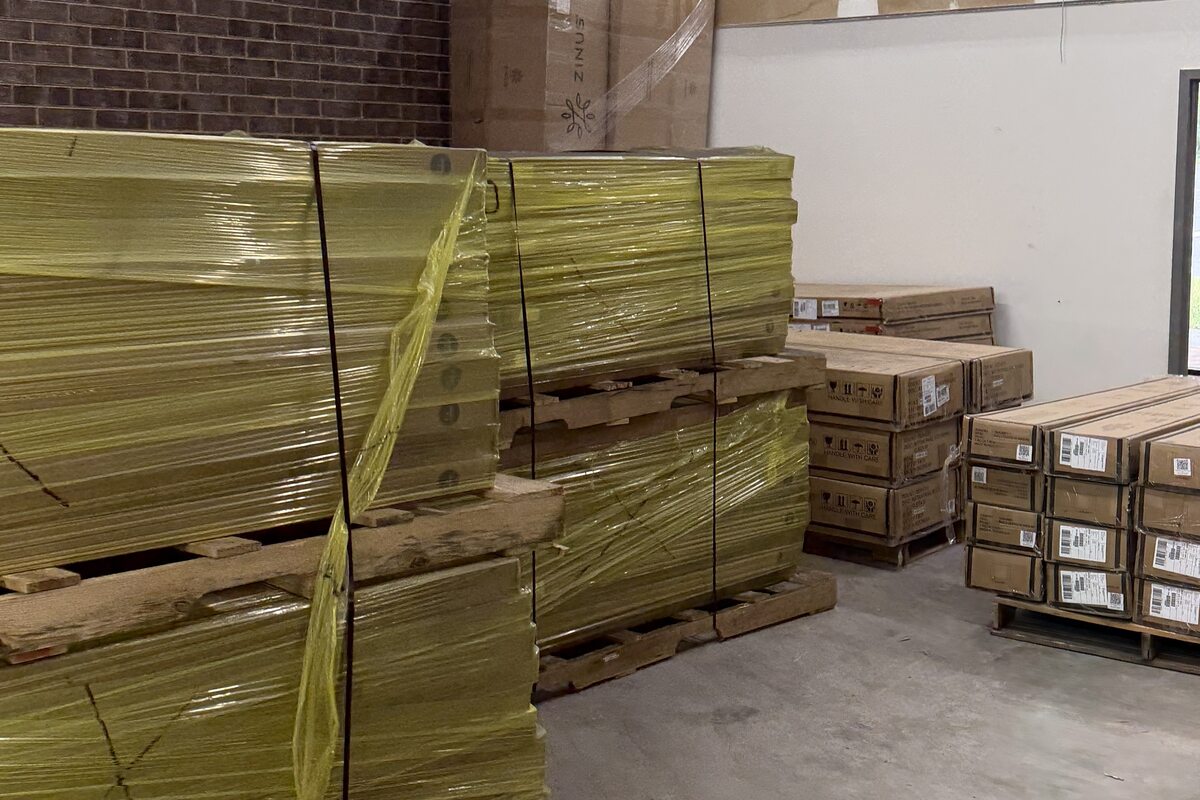 Pallets of bed frames banded in yellow strapping, with boxed stock stacked alongside.